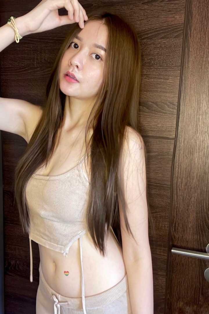 Young woman with long brown hair, wearing a beige crop top and pants.